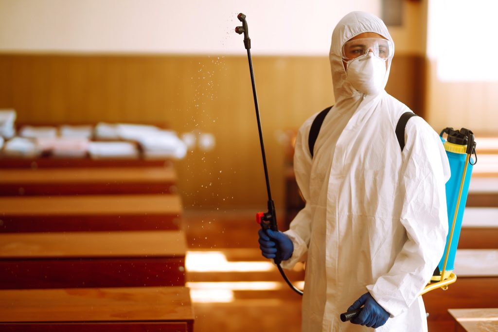 Portrait of man in protective hazmat suit with spray chemicals disinfecting school class. COVID-19.