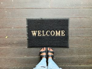Selfie of feet in sandals shoes with welcome mat on wooden floor